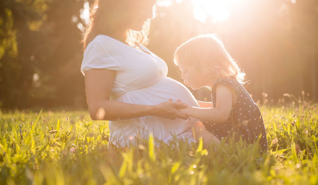 Child kissing mother's pregnant belly with sunshine in the background.