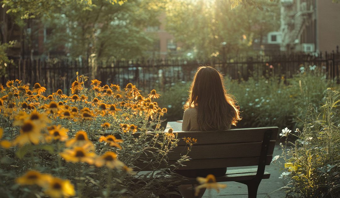 Woman sitting on a bench in a flower garden with sunshine.